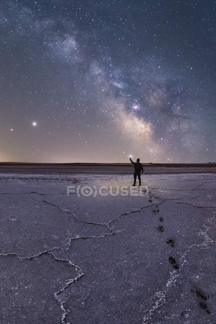 Силуэт исследователя, стоящего в сухой соленой лагуне с фонариком на фоне звездного неба с светящимся Млечным Путем ночью — стоковое фото