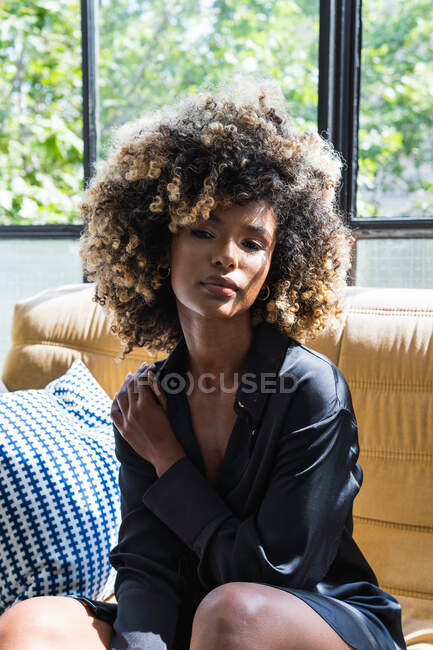 Tranquil African American female with curly hair sitting on comfortable  couch in living room and enjoying weekend at home — pleasure, black - Stock  Photo | #528440396