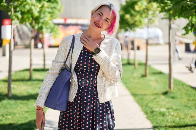 Entzücktes alternatives Weibchen mit gefärbten Haaren steht an einem sonnigen Sommertag auf der Straße und blickt in die Kamera — Stockfoto
