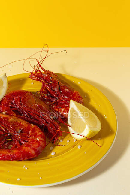 Fruits de mer savoureux de crevettes rouges cuites avec des tranches de citron frais et du sel grossier sur fond de deux couleurs — Photo de stock