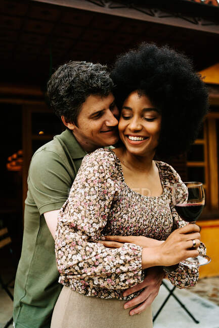 Couple multiracial positif debout près du porche du chalet et embrasser tout en profitant week-end ensemble — Photo de stock