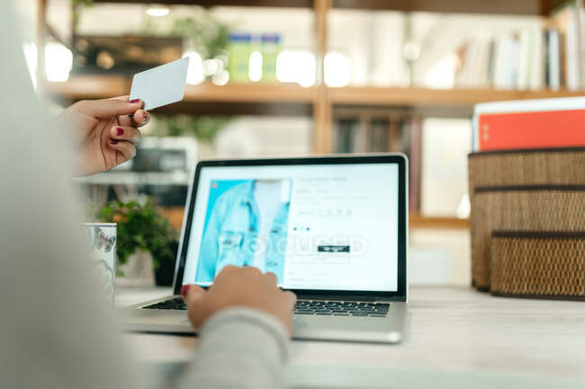 Cortar fêmea irreconhecível fazendo compra com cartão de plástico para a ordem durante as compras on-line via laptop — Fotografia de Stock