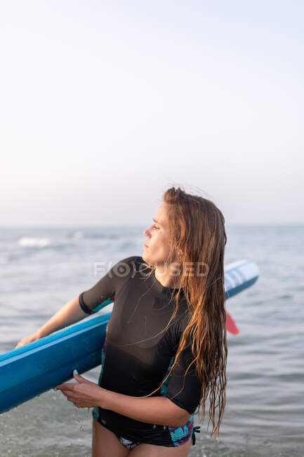 Weibchen im Badeanzug stehen im Sommer mit SUP-Board im Meerwasser und schauen weg — Stockfoto