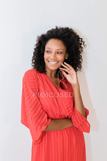 Усміхнена етнічна жінка з кучерявим волоссям у модному платті зі смугастим орнаментом, що дивиться — стокове фото