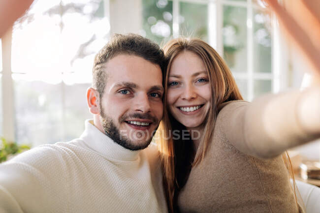 Allegro uomo barbuto con sincera donna amata scattare autoritratto mentre si guarda la fotocamera a casa — Foto stock