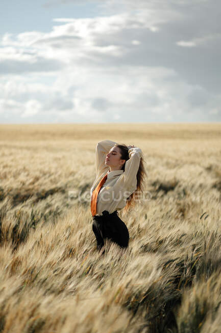 Вид сбоку на молодую внимательную женщину в формальной одежде с галстуком и закрытыми глазами среди шипов в сельской местности — стоковое фото