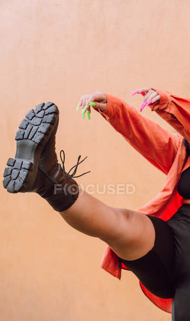 Side view full body of cheerful female millennial in stylish outfit kicking air against orange wall — Stock Photo