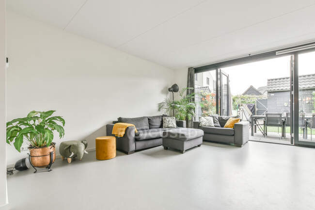 Diseño interior de moderno apartamento de espacio abierto con cómodos sofás en zona de salón cerca de gran ventana - foto de stock