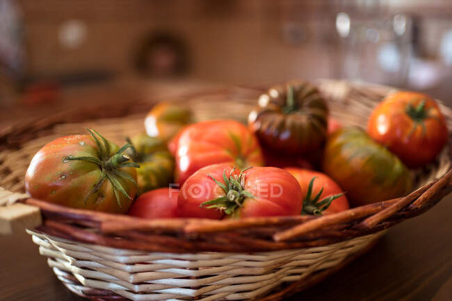 Pile of fresh tomatoes in wicker basket placed on table in rustic kitchen in harvest season — Stock Photo