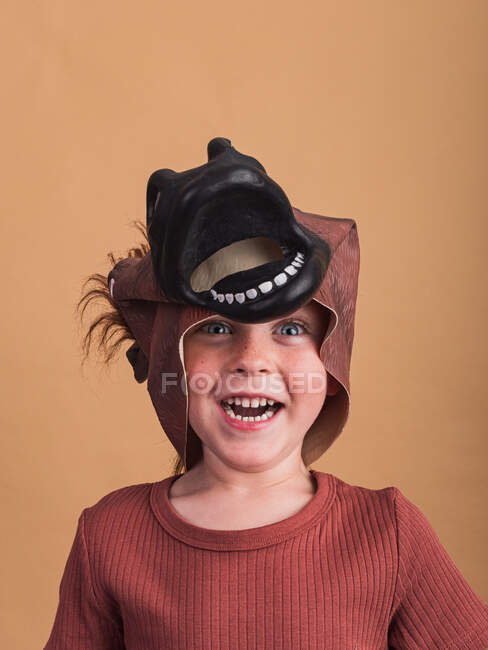 Bambino in t-shirt e maschera cavallo sulla testa guardando la fotocamera su sfondo beige — Foto stock