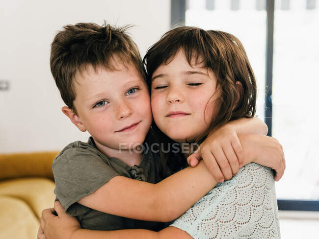 Милі змістовні близнюки, які ніжно обіймаються і сидять разом у вітальні вдома — стокове фото