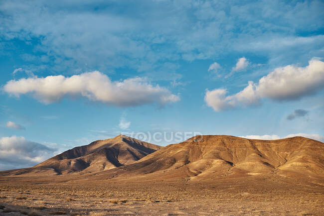 Nuages blancs flottant sur un ciel bleu vif au-dessus d'une vallée et de collines arides le jour d'été à Fuerteventura, Espagne — Photo de stock