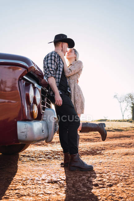 De baixo casal na moda no amor abraçando perto estacionado carro pickup retro vermelho no dia ensolarado no verão — Fotografia de Stock