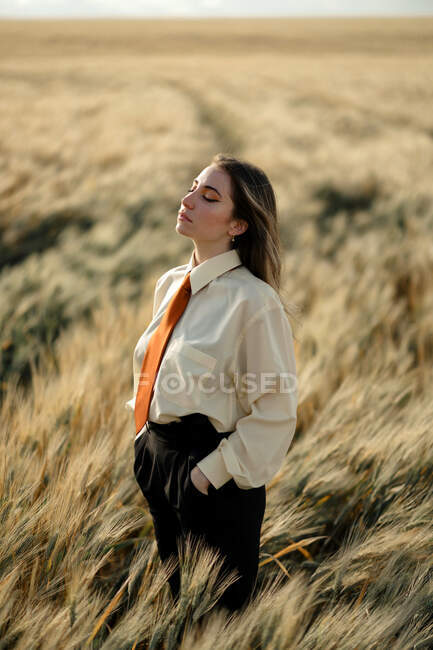 Vista laterale di giovane donna consapevole in abito formale con cravatta e occhi chiusi tra punte in campagna — Foto stock
