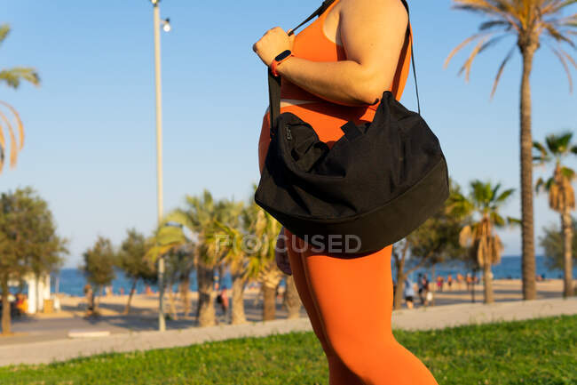 Side view of crop unrecognizable sportswoman with curvy body in active wear and smart watch standing on meadow in town — Stock Photo