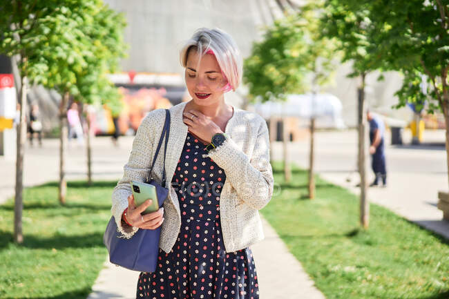 Fröhliche Alternative mit gefärbten Haaren, die im Sommer auf der Straße steht und mit dem Handy im Internet surft — Stockfoto