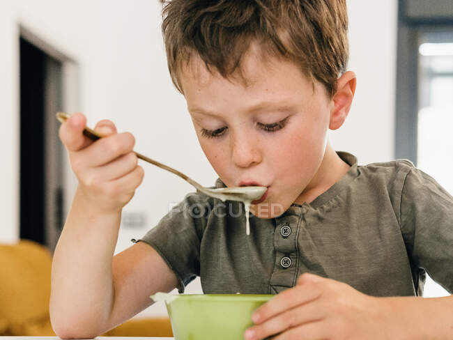 Adorable niño comiendo sopa de crema apetitosa con cuchara durante el almuerzo en casa - foto de stock