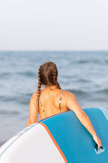 Back view of unrecognizable female in swimsuit standing with SUP board in sea water in summer — Stock Photo