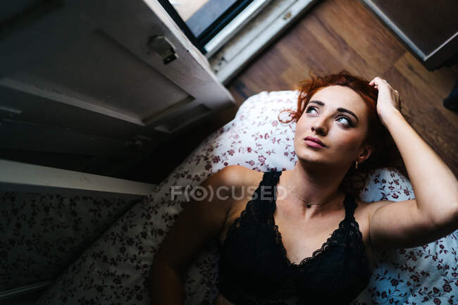 Top view of unemotional pretty redhead female lying on soft bed looking away at home — Stock Photo
