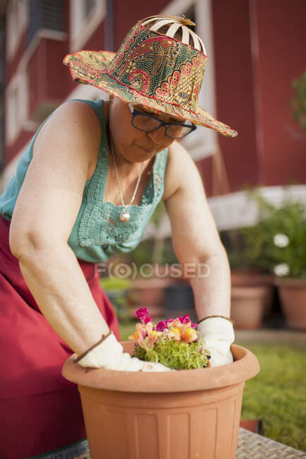 Vue latérale du jardinier femme mature, transfère une plante dans un grand pot de fleurs dans son jardin à la maison — Photo de stock