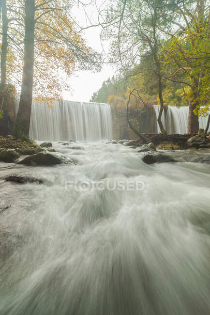 Scenic view of mount with cascades and river with foamy water fluids on stones between autumn trees in Lozoya, Madrid, Spain. — Stock Photo