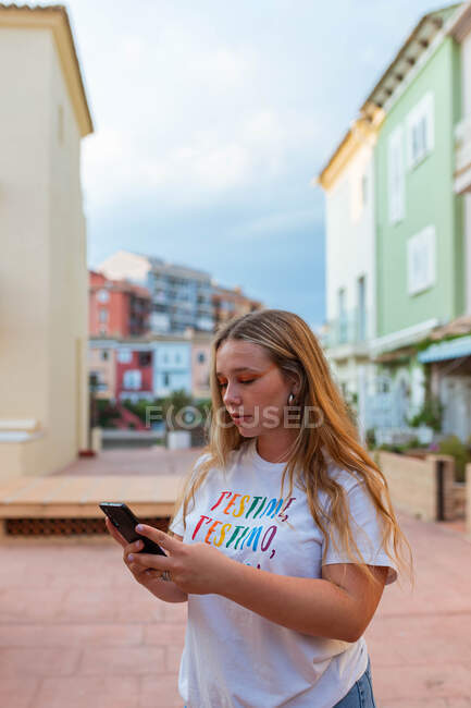 Jovem mulher na moda em pé na rua no verão e mensagens nas mídias sociais via telefone celular — Fotografia de Stock