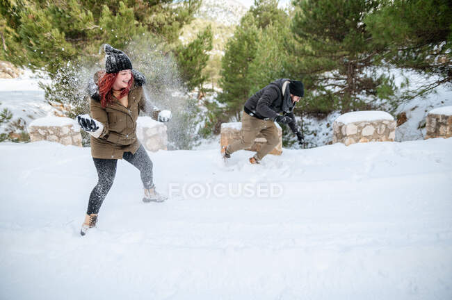 Cheerful friends in warm clothes playing snowballs in forest while enjoying winter day and having fun — Stock Photo