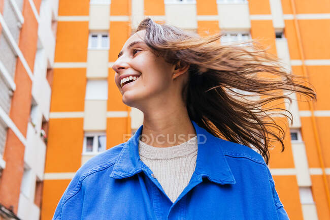 Baixo ângulo de fêmea alegre em pé na rua contra edifício brilhante e rindo — Fotografia de Stock