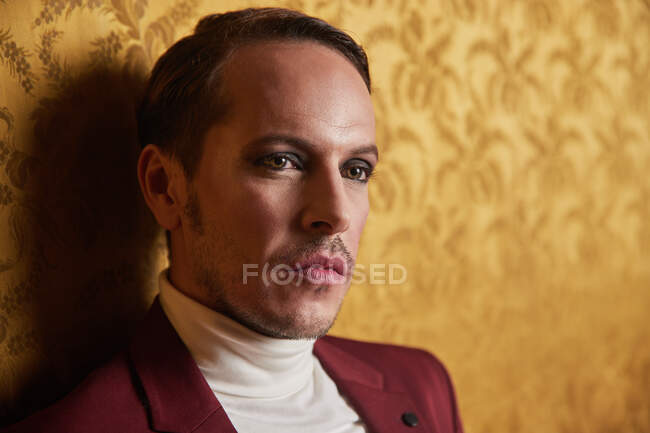 Confident adult male actor in elegant classy clothes looking away thoughtfully while standing near wall in vintage style room — Stock Photo