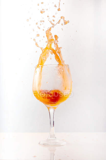 Освіжаючий апельсиновий коктейль, що бризкає у блискучому скляному горщику на сірому фоні в студії — стокове фото