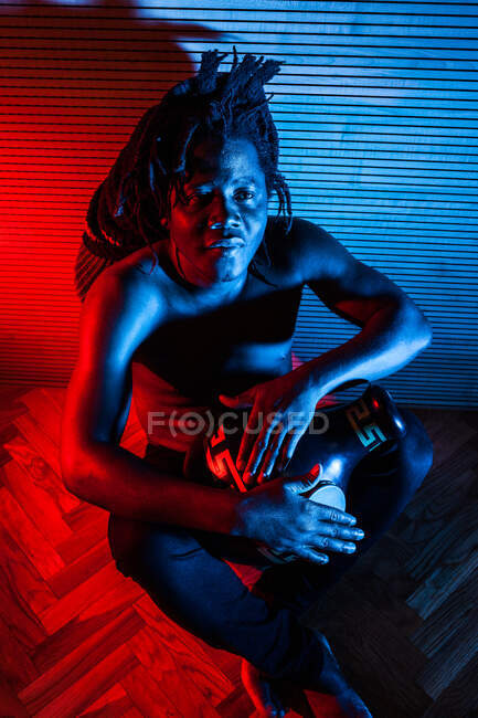 Мрійливий чорний музикант з голим тулубом грає африканський барабан у студії з червоними і синіми неоновими вогнями. — стокове фото