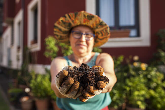 Reife Gärtnerin zeigt neue Erde für ihre Pflanzen in den Händen — Stockfoto