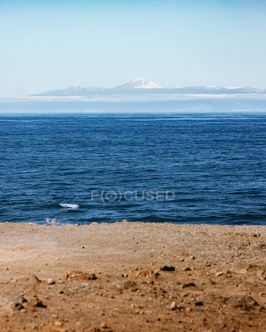 Amazing landscape of sandy shore and calm sea on background of mountain ridge under blue cloudless sky — Stock Photo