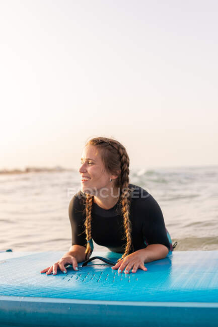Donna surfista deliziata sdraiata a bordo SUP e galleggiante sulle acque calme del mare nella giornata di sole — Foto stock
