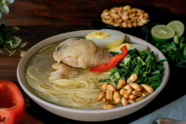 Du dessus de bouillon de poulet frais appétissant avec des ingrédients variés servis dans un bol sur la table dans la cuisine — Photo de stock