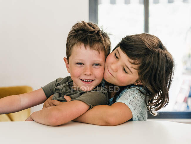 Conteúdo bonito gêmeos abraçando ternamente e sentados juntos na sala de estar em casa — Fotografia de Stock