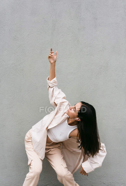 Ballerina spensierata che ascolta musica in cuffia e balla a occhi chiusi mentre si gode canzoni sullo sfondo del muro grigio in città — Foto stock