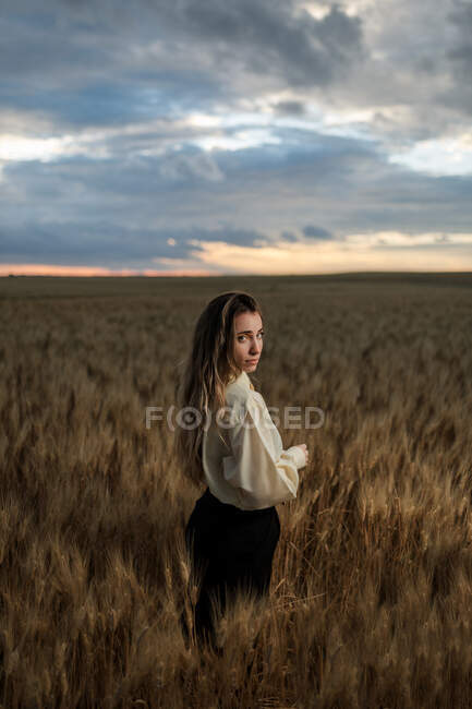 Vista lateral da jovem mulher consciente em desgaste formal com gravata olhando para a câmera entre picos no campo — Fotografia de Stock