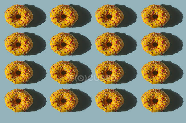 Vista superior de muchas rosquillas cubiertas con cubierta amarilla y bolas de colores sobre fondo azul - foto de stock
