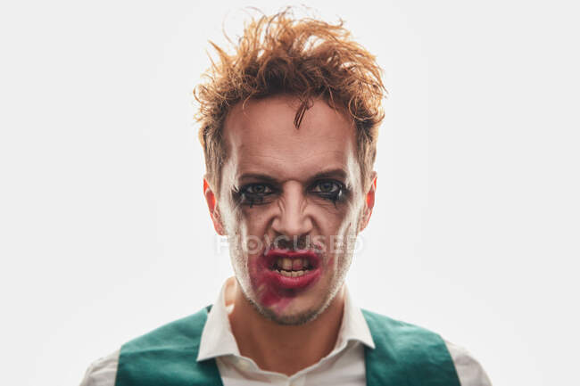Excéntrico sorprendido actor masculino con maquillaje untado actuando sobre fondo blanco - foto de stock