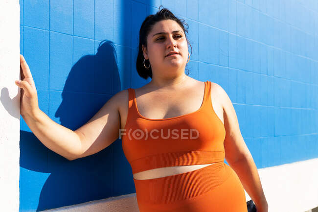Mujer atleta regordeta en ropa deportiva haciendo ejercicio en la pasarela de baldosas en la ciudad soleada - foto de stock
