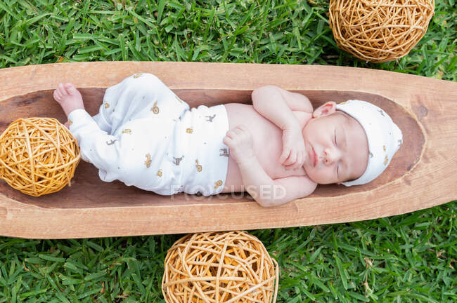 Top view of cute small newborn baby sleeping while lying in wooden tub placed on green grass — Stock Photo