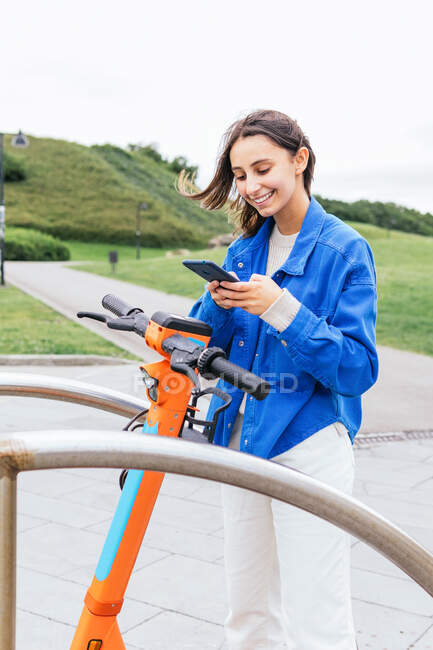 Contenuto femminile noleggio scooter elettrico parcheggiato in città e la navigazione cellulare — Foto stock