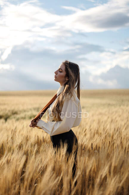 Side view of young mindful female in formal wear with tie and closed eyes among spikes in countryside — Stock Photo
