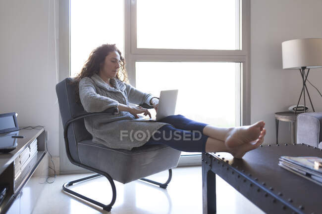 Seitenansicht einer Geschäftsfrau mit lockigem Haar, die auf dem Sofa sitzt und mit ihrem Laptop arbeitet — Stockfoto
