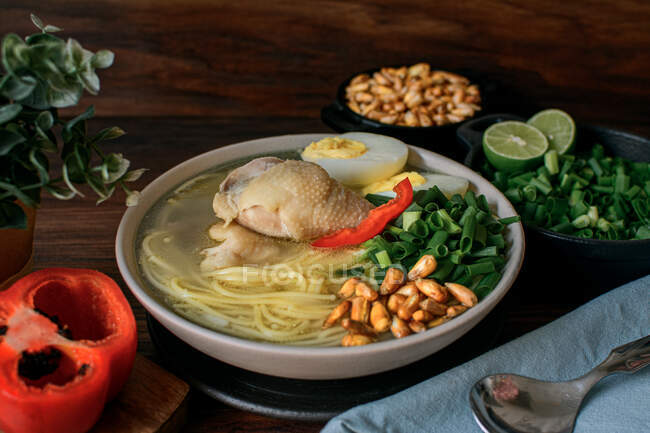 Desde arriba de apetitoso caldo de pollo fresco con ingredientes variados servidos en un tazón en la mesa en la cocina - foto de stock