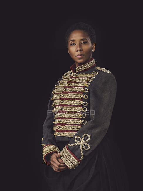 Senhora adulta afro-americana confiante em jaqueta elegante olhando para a câmera no estúdio escuro no fundo preto — Fotografia de Stock