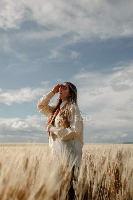From below side view of young mindful female in formal wear with tie and closed eyes among spikes in countryside — Stock Photo