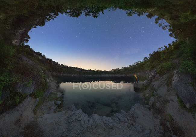Viaggiatore anonimo con torcia che contempla la laguna tra le montagne sotto il cielo stellato al tramonto in Spagna — Foto stock