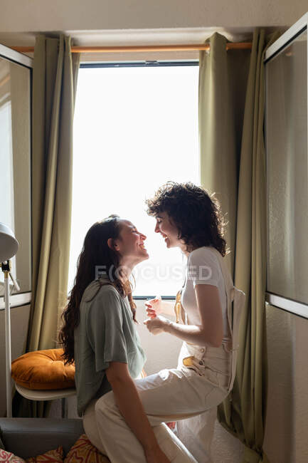 Vista laterale del contenuto Coppia LGBT di donne innamorate sul divano di casa e che si guardano con amore — Foto stock